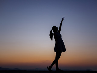 Silhouette of a young dancing woman with long wavy hair in the mountains , Natural light and darkness,against the background of the sunset sky.