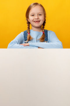 Happy cheerful child holds a blank white banner of space on a yellow background