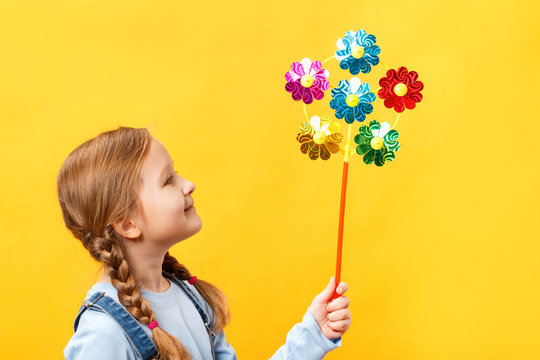 Cute beautiful child holding a pinwheel toy. Little girl close-up on a yellow background