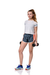 A young caucasian girl in workout shorts & a white t-shirt holding dumbbells standing isolated on a white background