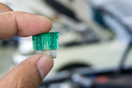 Man hand holding Automotive blown fuse on blurred car in repair shop on background.	