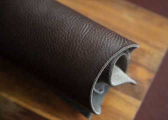 Brown leather in roll. Roll of brown color leather. Materials for leather craft. Copy space. Handmade craft. Samples of leather on wooden background