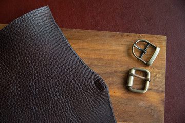 Leather working or Leather craft. Brown italian leather on leather craftman's work desk . Two buckle on wood background.