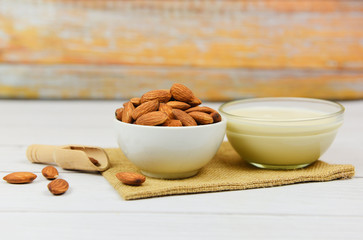 Almond milk in bowl and almonds on wooden scoop on sack