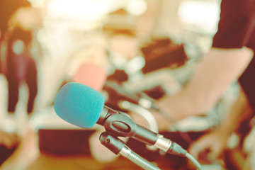 Two microphones with blue and red sponges placed on a stand with earphones on the table with blur image of the audio technician was installing and testing the sound system in the background.