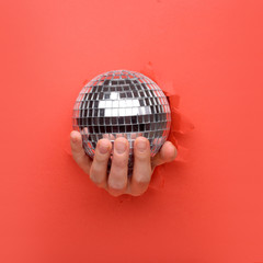 Hand holding Silver disco mirror ball on torn red paper wall. Copy space aside for your advertising and offer or sale content.
