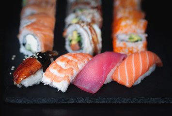 Japanese nigiri sushi and rolls with unagi, srimp, tuna and salmon on black stone plate.