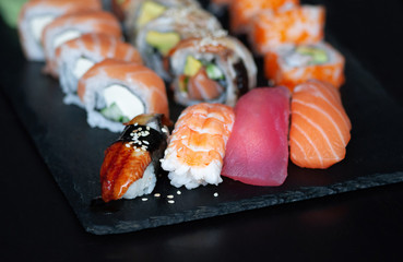 Sushi set with nigiri sushi, uramaki California, Philadelphia, Unagi rolls on black slate plate.