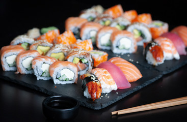 Sushi set with nigiri sushi, uramaki California, Philadelphia, Unagi rolls on black stone plate.