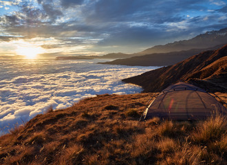 A small tent without an awning, on the edge of a high hill along the route to the eastern base camp of Mardi Himal. Stunning sea view of clouds at sunset