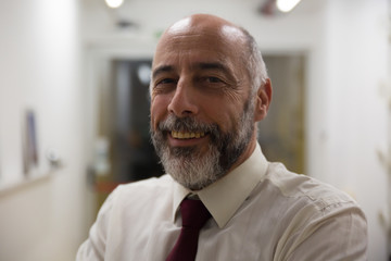 Fototapeta premium Cheerful mature businessman smiling at camera. Close-up portrait of happy bearded businessman standing in office and looking at camera. Leadership concept