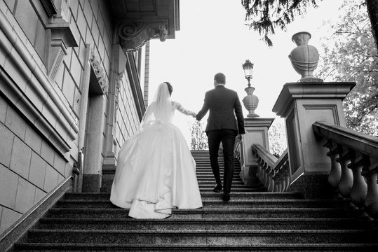wedding couple (woman and man) in wedding dress and suit walking on the castle stairs outdoor. Love, family, tenderness concept