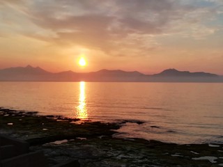 the sun setting behind the promontory with the sea in the foreground