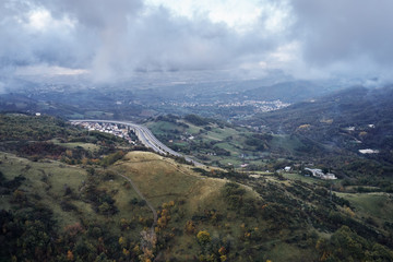 Autumn alpine speed road in Italia. Aerial view from above with clouds on the background and village far away