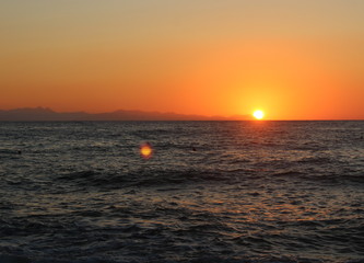 the sun setting behind the promontory with the sea in the foreground