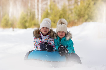 Joyful girls ride a tubing from a hill together. Winter holiday.