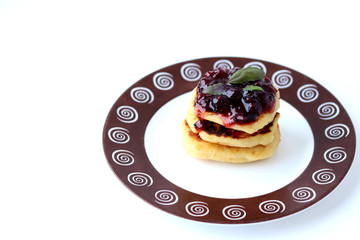 Cheesecakes stacked on top of each other, watered with blueberry jam, decorated with Basil leaves on a plate with a pattern on a white background.Side view