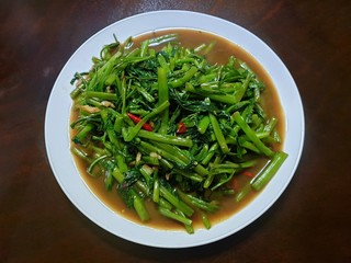 Top view of fried water spinach seasoned with chili and soy sauce on wooden table as a background, Stir fried swamp cabbage or chinese morning glory, Pad pak boong is Thai traditional, Ready to eat