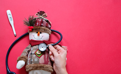 Doctor and christmas concept. Sick snowman and stethoscope on red background with place for text.
