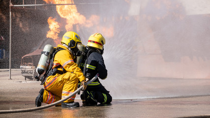 The back view of two firefighters practicing using fire-fighting water that is burning
