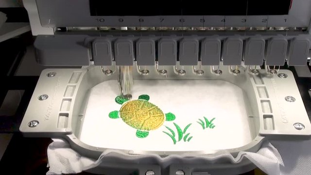 start  and stop of work of the embroidery machine with the green  thread   when performing work on the automated production of a colored design turtle and  grass on the white  background