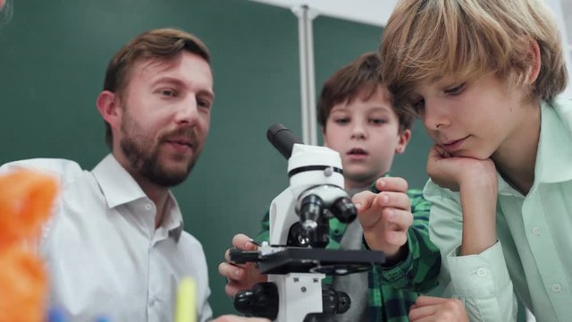 lesson in a modern school, a teacher and children's look into a microscope, studying biology and chemistry in school.