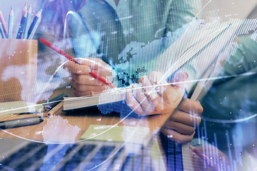 Fototapeta premium A woman hands writing information about stock market in notepad. Forex chart holograms in front. Concept of research. Multi exposure