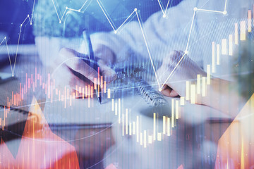 Financial forex graph displayed on hands taking notes background. Concept of research. Double exposure