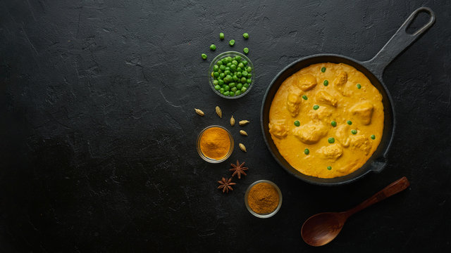 Cooking tasty chicken curry in pan on black background. Flat lay, top view with copy space