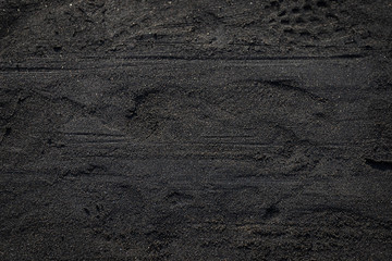 Black sand texture on the beach with some footprint on surface, full of pebble spread around