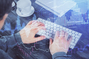 Multi exposure of graph with man typing on computer in office on background. Concept of hard work.