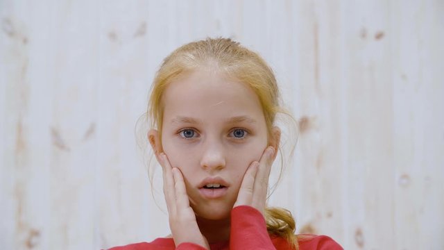 Surprised girl with opened mouth and eyes touching face front camera on light background. Shocked teenager girl from amazement holding face to hands. People emotion concept