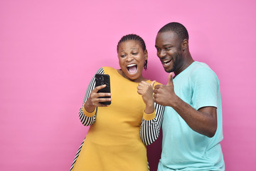 young black man and woman feeling excited and happy viewing content on a mobile phone together,...