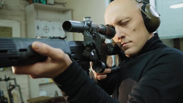 A man looks into the optical sight of a sniper rifle in a shooting gallery, takes aim at a target