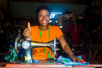 young african woman who is a tailor working on a dress smiling, gives a thumbs up