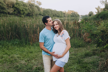Portrait of a young family expecting a baby. Loving man and beautiful pregnant blond woman cuddling against the backdrop of greenery in the park. Pregnancy picture, concept.