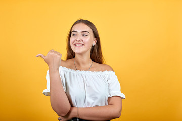 Young brunette lady pointing aside, smiling, looking happy isolated on orange background in studio...