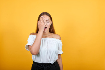 Tired young woman covered eye with hand, opened mouth , looking sleepy isolated on orange background in studio in casual white shirt. People sincere emotions, lifestyle concept.