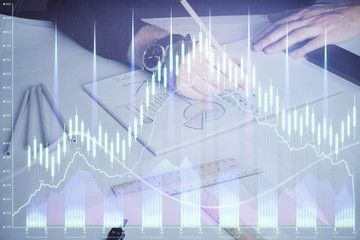 Double exposure of man's hands writing notes of stock market with forex chart.