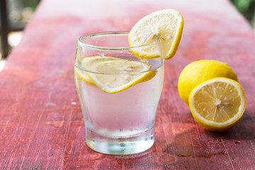 A glass of lemonade and cut lemon on a red table