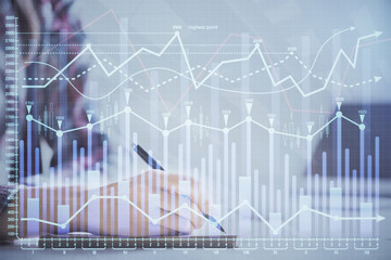 A woman hands writing information about stock market in notepad. Forex chart holograms in front. Concept of research. Double exposure