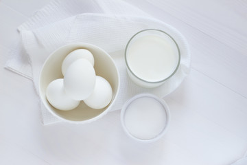 four white eggs lie in a plate on a white wooden table next to a towel and a glass of milk and a salt shaker.