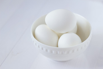four white eggs lie in a plate on a white wooden table.