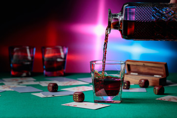 Casino table with cards and dice . Whisky is poured into a glass from a decanter .
