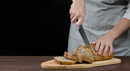 Female hands slicing home-made bread. Isolated on dark background. Empty space for text