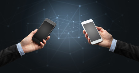 Close up of two hands holding smartphones to each other, wireless connection concept