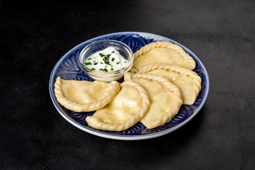 Dumplings with sour cream on a blue plate shot on a black background