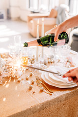 New Year 2020. New Year mood. Table with a gold tablecloth, decorated with candles and tableware for celebration. Festive still life by candlelight.A man pours champagne into a glass. Close-up.