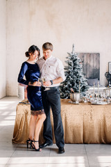 Obraz premium Man and woman clink glasses champagne near the New Year's table for Christmas. Couple celebrating New Years Eve 2020.