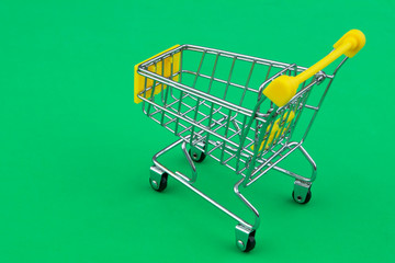 Yellow shopping cart or trolley on green background close up